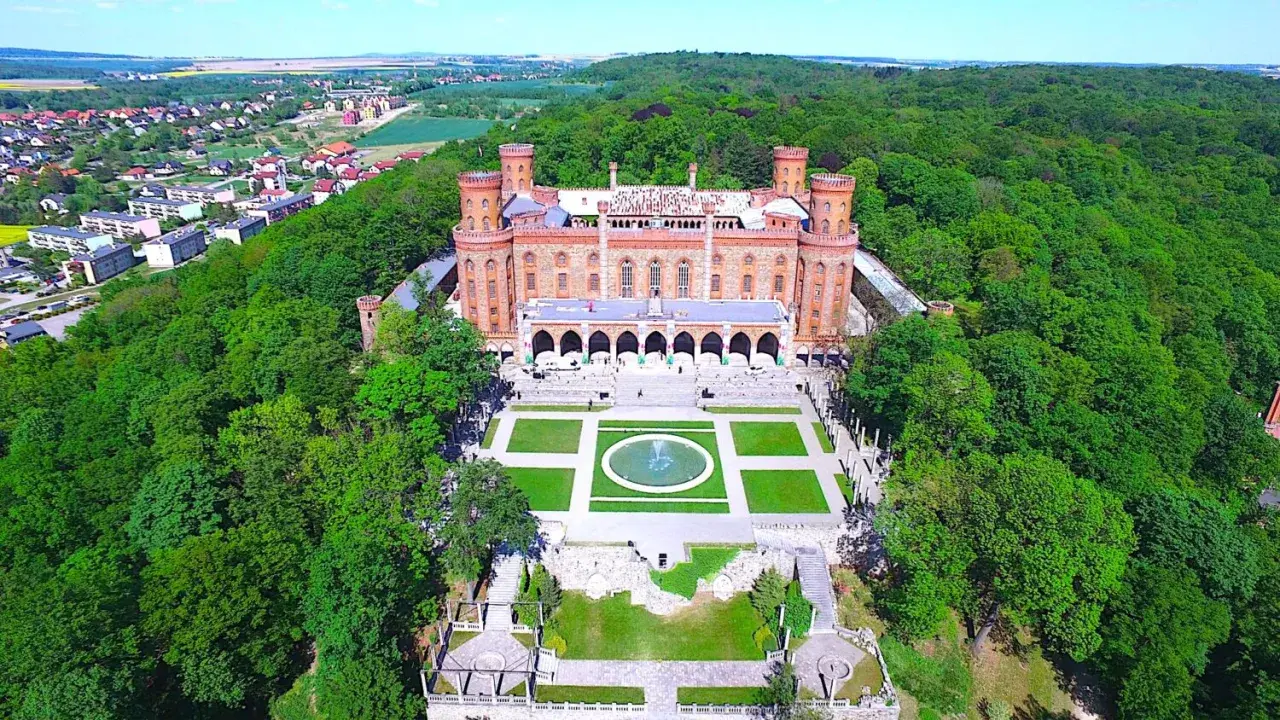 Kamieniec Ząbkowicki zamek, otoczony bujną zielenią, prezentuje swoją neogotycką architekturę z wieżami i arkadowym dziedzińcem.