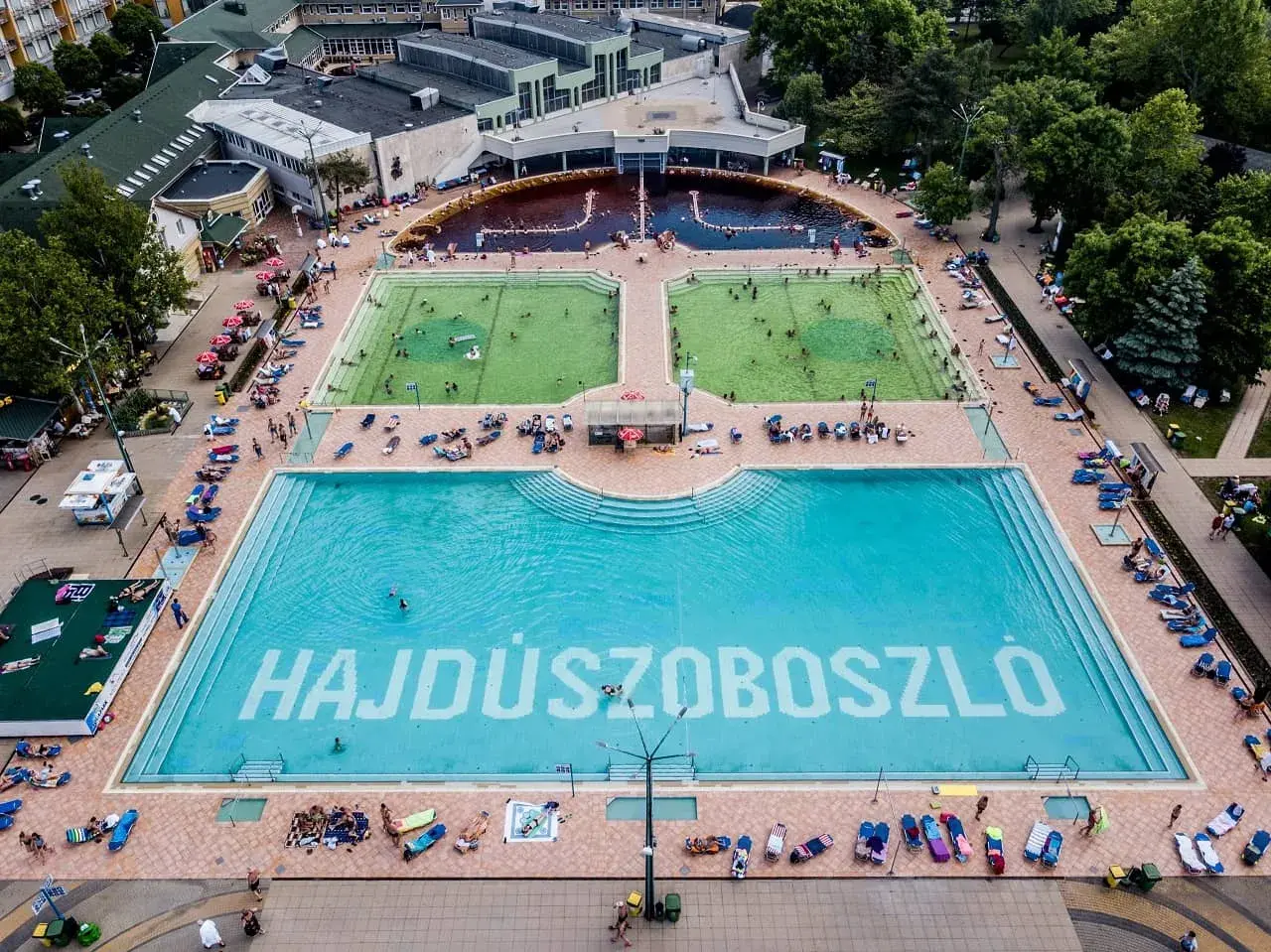Hajdúszoboszló baseny cennik: aerial view of a large complex with multiple pools, including a vast blue pool with "HAJDÚSZOBOSZLÓ" written on the bottom.