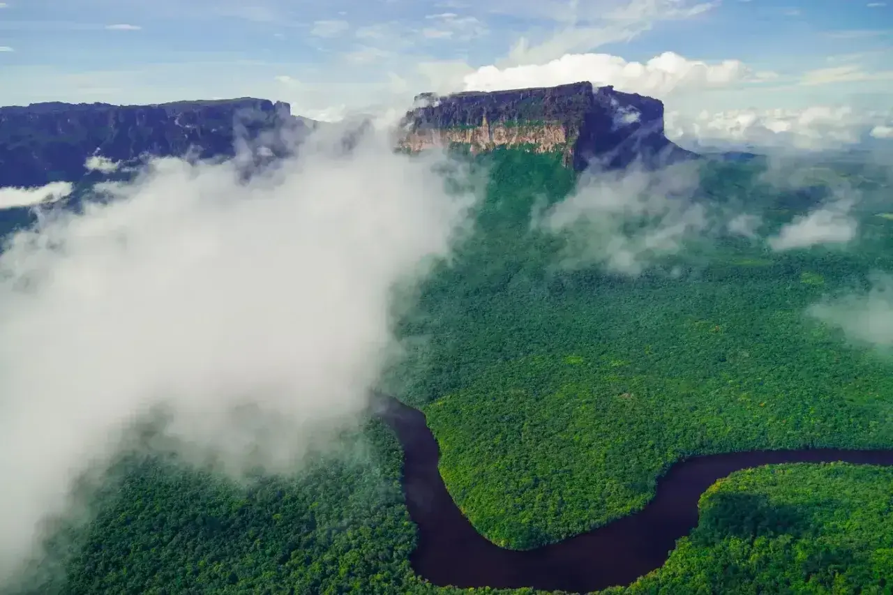 Mgliste chmury otulają zielony las i krętą rzekę, odsłaniając majestatyczne góry. Widok jak z **Angel Falls**.