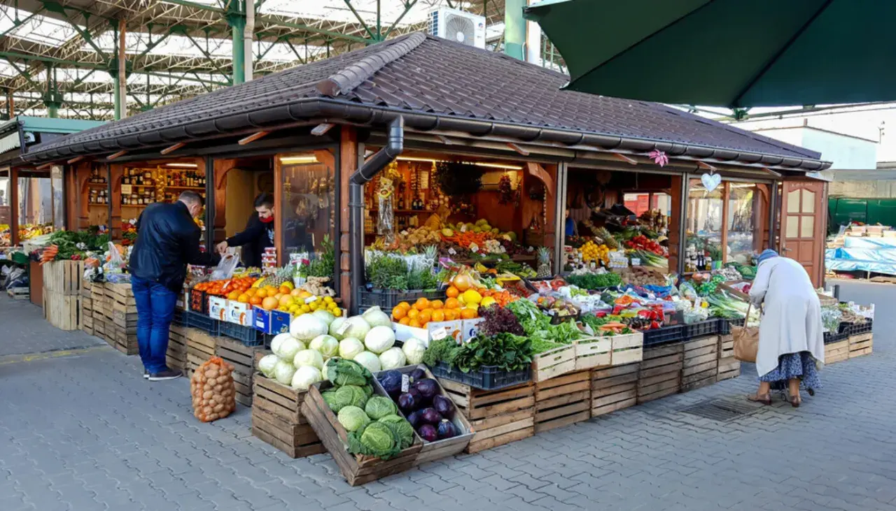 Kolorowy stragan na Kleparzu pełen świeżych warzyw i owoców. Klienci wybierają produkty, tworząc tętniącą życiem scenę.