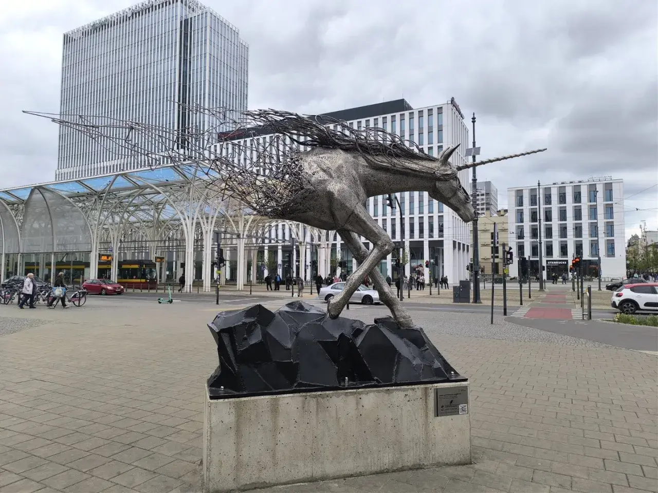 Metalowy jednorożec na skalnej podstawie, symbolizujący dynamikę i nowoczesność, na tle architektury Piotrkowska Łódź.