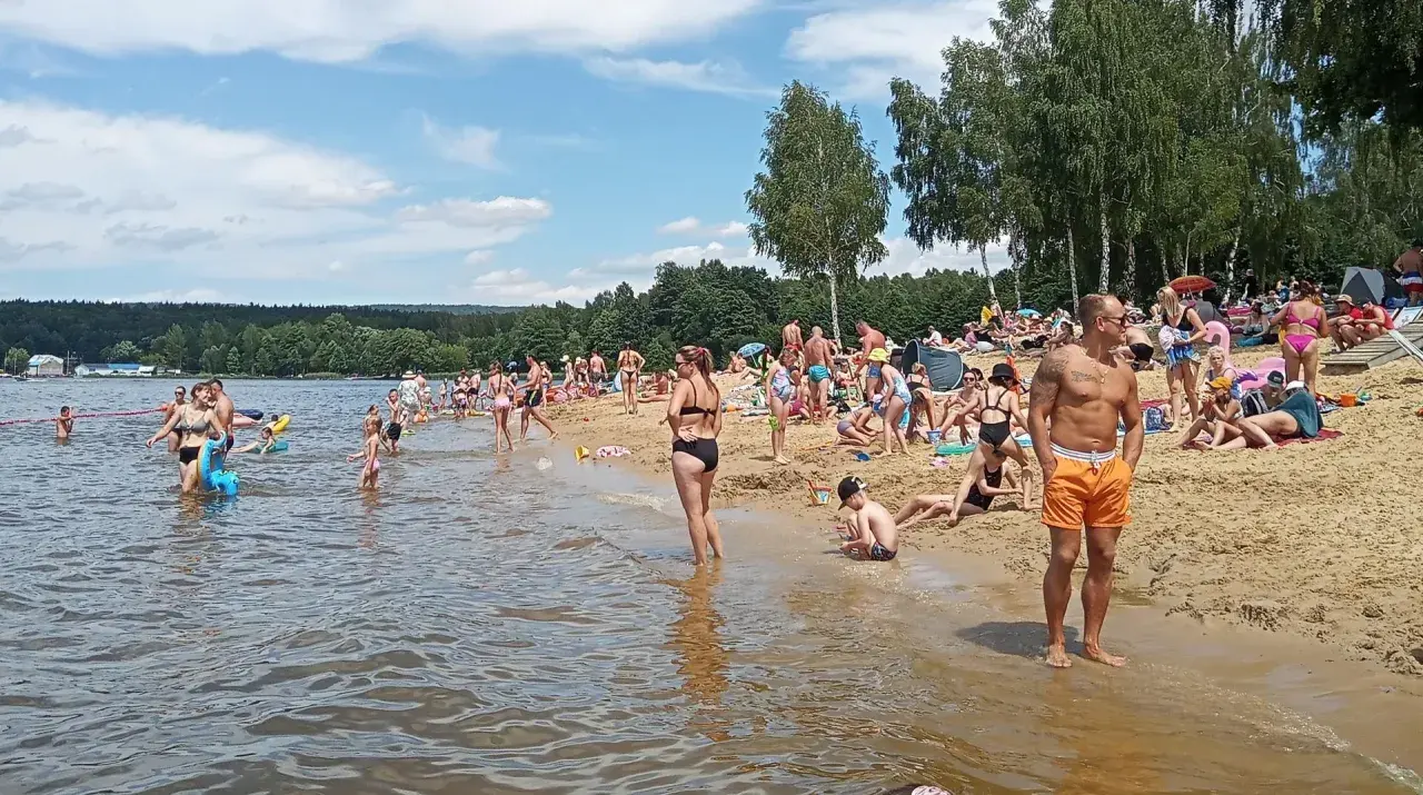 Tłumy ludzi korzystają z kąpieliska, plaży i wodnych atrakcji w słoneczny dzień.
