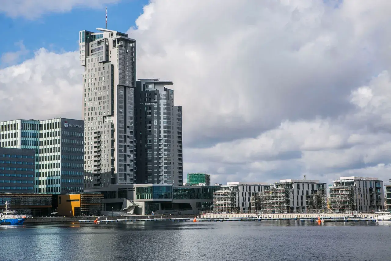 Nowoczesne sea towers w Gdyni, zdominowane przez szare i białe fasady, odbijają się w spokojnej wodzie portu.