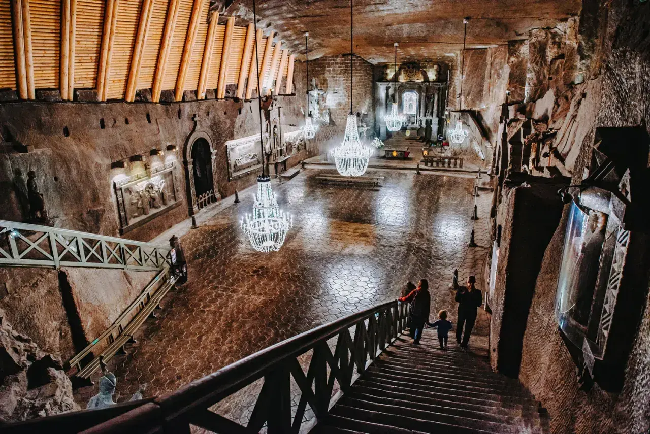 Wielka komora w kopalni soli Wieliczka, z kryształowymi żyrandolami i turystami schodzącymi po schodach. Sprawdź kopalnia soli Wieliczka cennik.