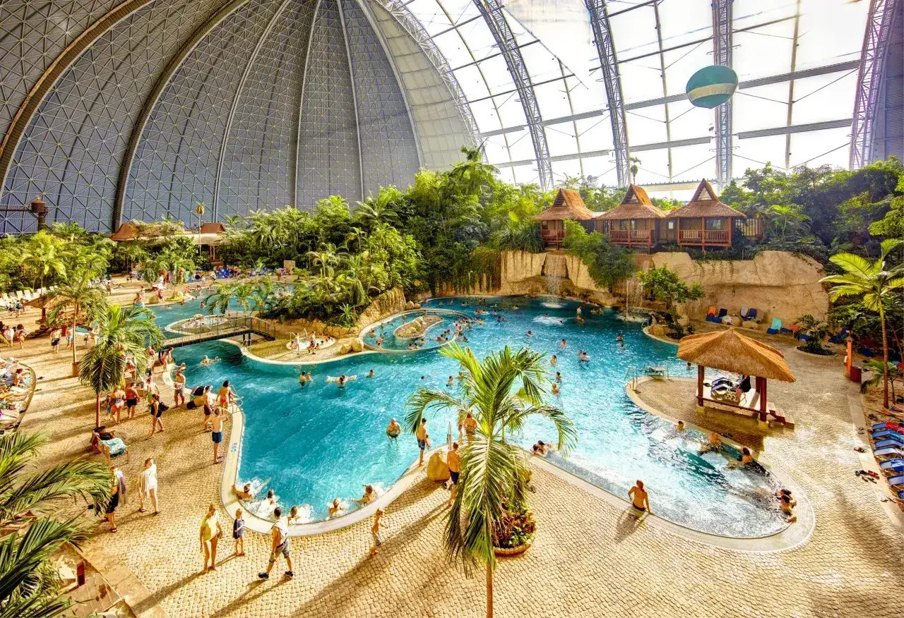 Wielki tropikalny basen pod kopułą, z palmami, domkami i ludźmi. Sprawdź nasz tropical island cennik, by zaplanować wakacje!