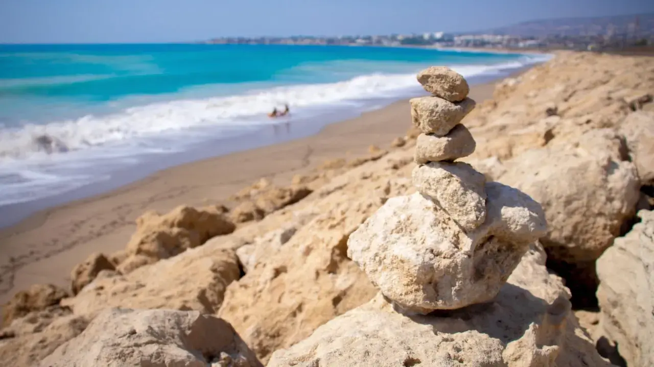 Kamienna wieża na plaży w Kato Pafos, z turkusowym morzem i falami w tle.