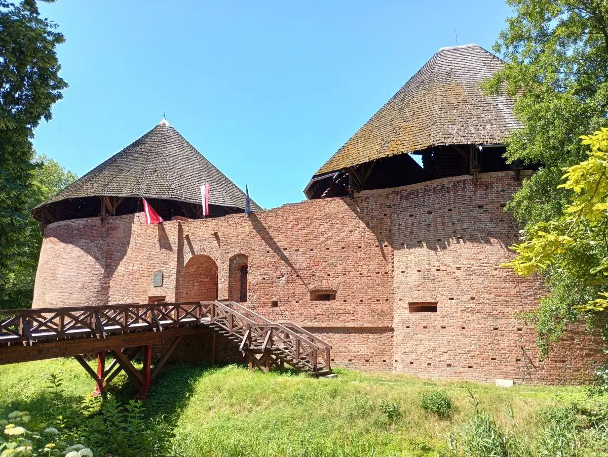 Zamek międzyrzecz z drewnianym mostem i schodami prowadzącymi do ceglanych baszt pod strzechą.