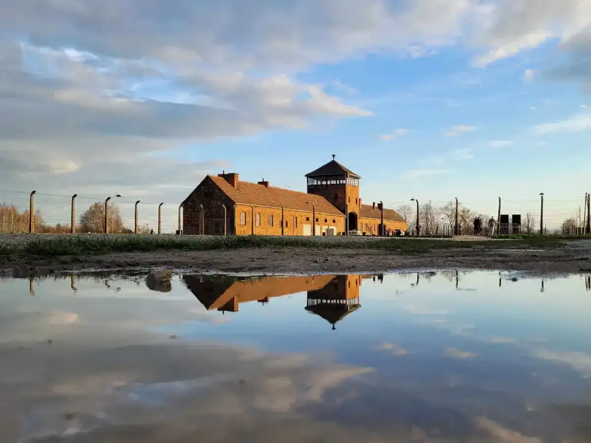 Odbicie ceglanego baraku z wieżą strażniczą w kałuży. To miejsce, gdzie jest Auschwitz, przypomina o historii.
