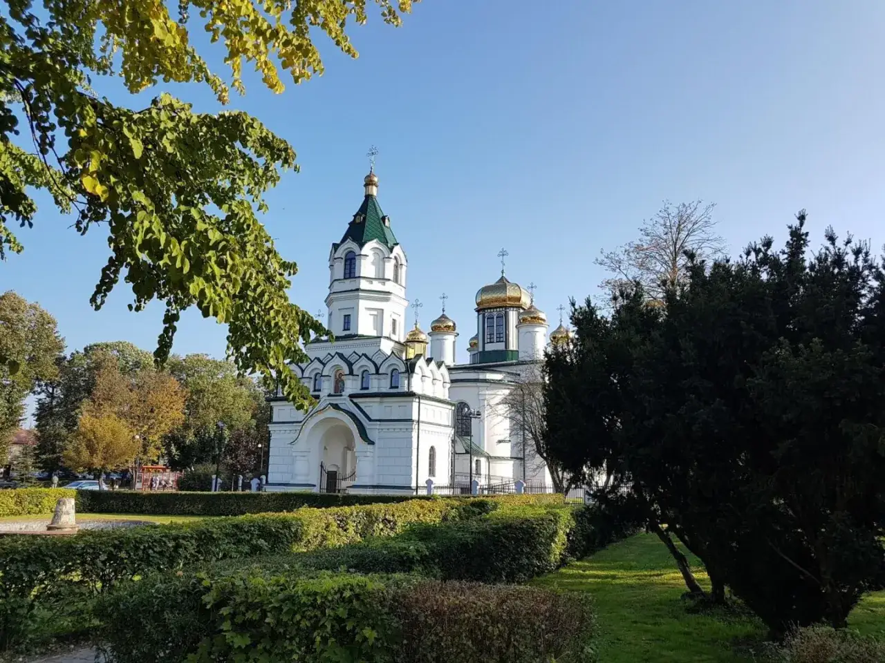 Biała cerkiew z zielonym i złotymi kopułami, otoczona zadbanym ogrodem. Jedna z pięknych sokółka atrakcje.