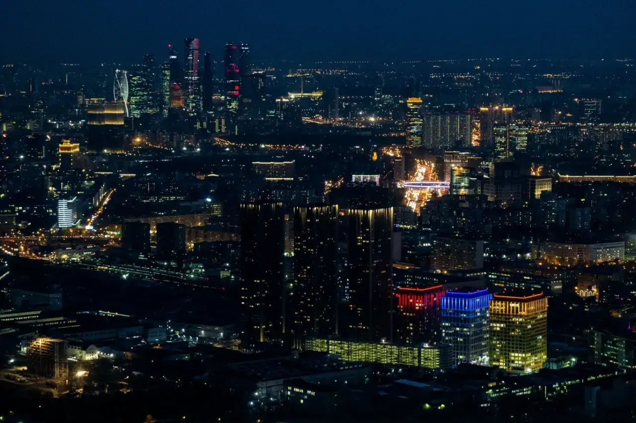Nocny widok na Moscow City, z oświetlonymi drapaczami chmur i rozświetlonymi ulicami, tworzącymi tętniący życiem krajobraz.
