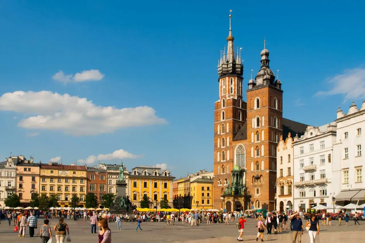 Rynek Główny w Krakowie, gdzie tętni życie. W tle Bazylika Mariacka i kolorowe kamienice.